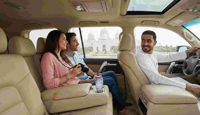 A private tour guide showing landmarks to a couple standing near a luxury car, illustrating the comfort and exclusivity of an Abu Dhabi Layover Tour from Airport.