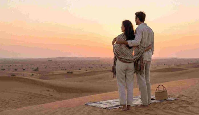 A couple dressed in elegant, comfortable attire enjoying an Anniversary & Honeymoon Dune Dinner Abu Dhabi, seated at a beautifully lit private table under the stars.