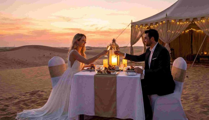 A couple toasting at a private candlelit table with a personal chef and Bedouin tent under the stars, depicting a romantic Anniversary & Honeymoon Dune Dinner Abu Dhabi.