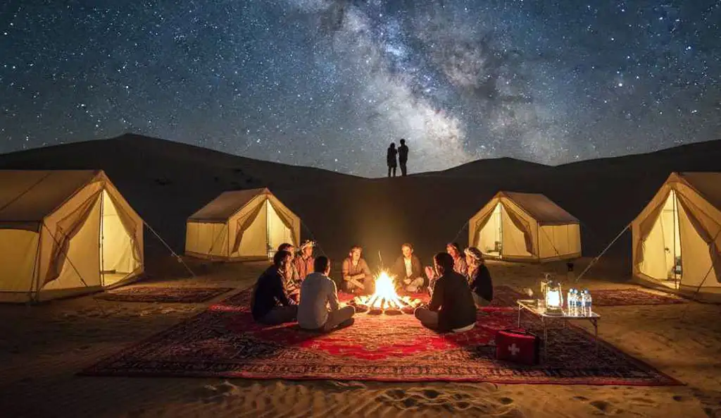 A group of travelers following safety tips for overnight desert safari Abu Dhabi by staying together near a well-lit campfire, with a first-aid kit visible and organized tents under a clear starry sky.