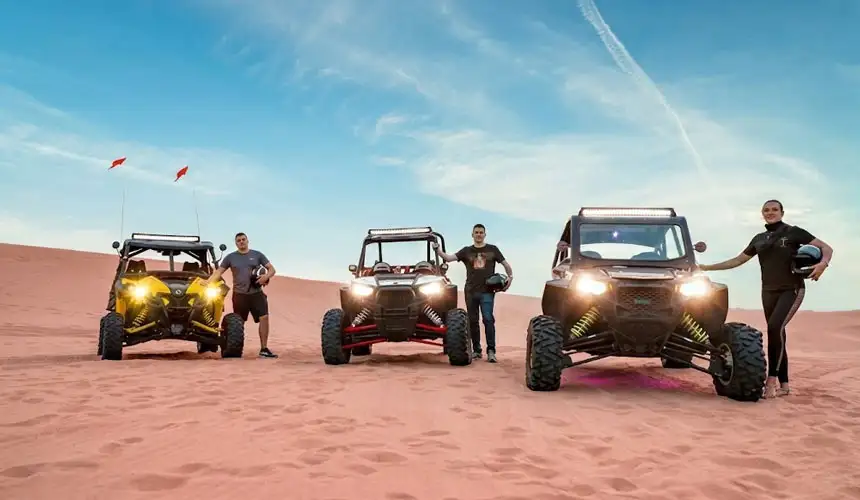 Group of yellow, black and red Polaris dune buggies with drivers posing in the golden sands of Abu Dhabi desert during a guided dune buggy tour experience.