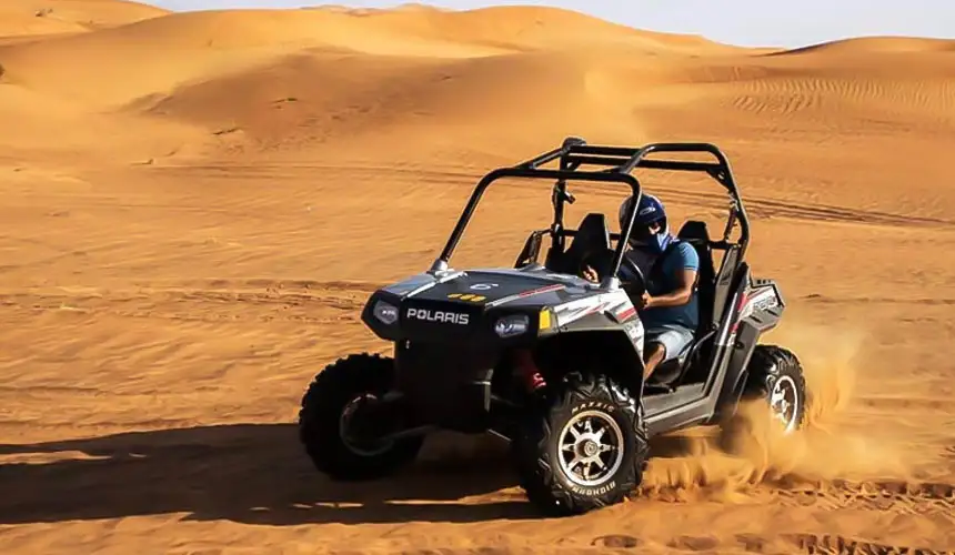 Black Polaris RZR dune buggy carving through the Abu Dhabi desert dunes creating a trail of flying sand during an thrilling off-road desert adventure.