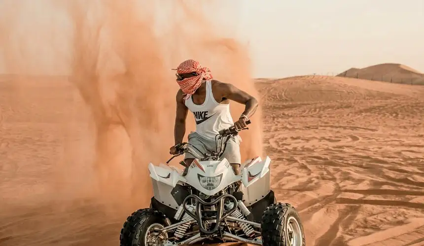 Powerful action shot of a rider performing a thrilling sand drift on a white quad bike during a desert quad bike tour in Abu Dhabi. Dynamic desert adventure with dramatic sand spray.